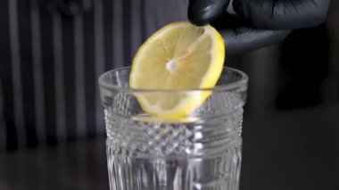 Cama limon ekle. Limonata yapmak, yaz içkisi, soğuk içecek, sağlıklı sıvı. Bir bardağa bir dilim limon at kadın elinin limon dilimini kapat içine su ve mavi bardakta buz koy. 