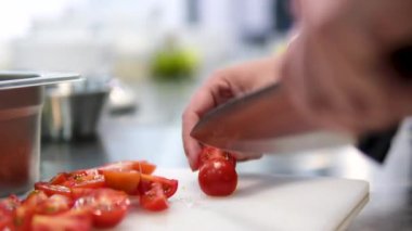 Evde Yunan salata hazırlığı için kadınların elleri vişne domateslerini dilimliyor. Domatesleri dilimle.