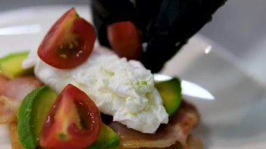 Eggs Benedict dish with hollandaise sauce cutting with fork and knife in outdoor restaurant. Classic breakfast meal with poached eggs, bacon on English muffin. Delicious and mouthwatering look of dish