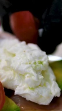 Eggs Benedict dish with hollandaise sauce cutting with fork and knife in outdoor restaurant. Classic breakfast meal with poached eggs, bacon on English muffin. Delicious and mouthwatering look of dish