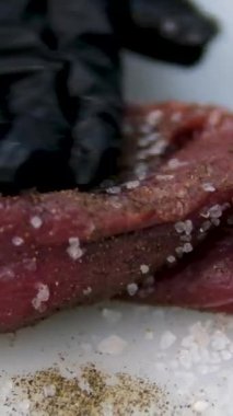 Şef biftek pişiriyor, arka planda profesyonel mutfağa tuz serpiştiriyor, ağır çekimde. Tuzlu sığır filetosu