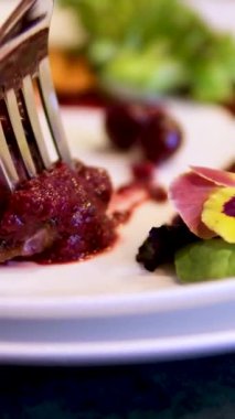 Beyaz tabakta servis edilen vişne soslu geleneksel yaban tavşanı filetosu yiyen kadın ellerinin yakın çekimi. Kiraz soslu dana eti.