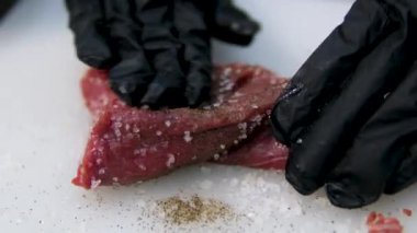 Şef biftek pişiriyor, arka planda profesyonel mutfağa tuz serpiştiriyor, ağır çekimde. Tuzlu sığır filetosu