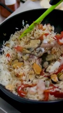 Paella geleneksel İspanyol yemekleri. İnsan kızartma tavasından tabağa deniz mahsulü paella koyar. Midyeli paella, Kral karidesleri, langoustine ve mürekkep balıklarıyla. Paella pişiren kişi. Akşam yemeği. 4K