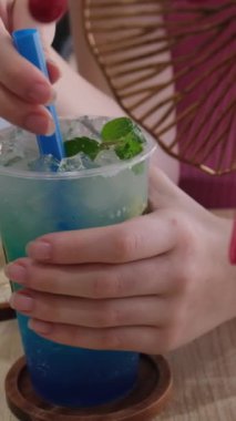 Limonata ve nane yapraklarıyla dönen bir bardak ve düşen bir buz küpünden su sıçratıyor. Mavi içecek naneli soğuk içecek naneli ve buzlu bardakta mavi pipetli çimenlikte.