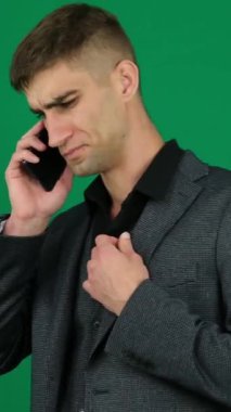 İş adamı cep telefonuyla konuşuyor. Yeşil arka plandaki yakışıklı bir adamın ciddi telefon konuşması duyguları. 