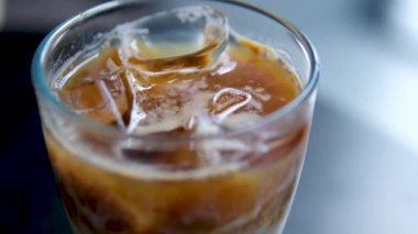 Süt, koyu bir masada buzlu kahveye dökülüyor.