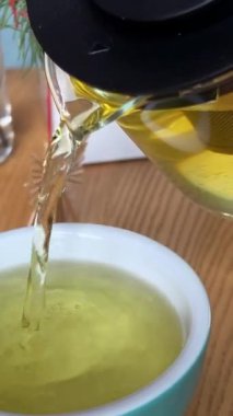 Portakallı, limonlu ve limonlu çayı şeffaf çaydanlıktan bardağa doldurmak. Arka planda bal ve krep ile çay demlemek. Yavaş çekim çayı. Bitki çayı dök.