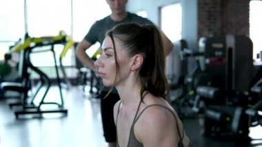 Genç ve güzel kaslı sporcu kız halter kullanarak modern bir spor salonunda egzersiz yapıyor. Kız spor salonunda çömeliyor.