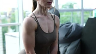 Genç ve güzel kaslı sporcu kız halter kullanarak modern bir spor salonunda egzersiz yapıyor. Kız spor salonunda çömeliyor.
