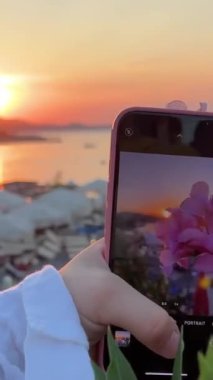 Sahilde çiçekleri fotoğraflamak. Arnavutluk video çiçekleri, deniz arkası telefon, kırmızı çiçek blogcusu kız eli çekti