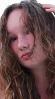 Kumsalda saçını düzelten genç bir kızın kumsaldaki duygularını dinlendiren yanık cilt kızıl yanakları ıslak saçlar. yüzme yaz tatili. Gölün arka planında bir kadın