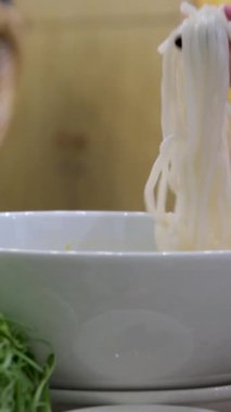 Vietnamlı çorbacı kızların elleri çubuklu pilav eriştelerini alıyor ve geleneksel lezzetli yemekler yiyorlar. Geleneksel Vietnam et çorbası.