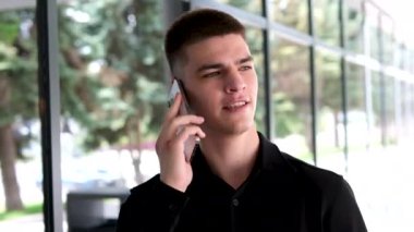 Siyah saçlı ve mavi gözlü yakışıklı bir adam. Melez ırk uyruğu. Ofisin yakınında telefonla konuşan bir adam.