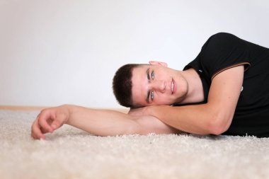 Siyah saçlı ve mavi gözlü yakışıklı bir adam. Melez ırk uyruğu. Adam yere yatmış, eline yaslanmış.