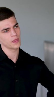 Yakışıklı, siyah saçlı ve mavi gözlü adamın tatminsiz yüzü. Melez ırk uyruklu yeşil gömlekli genç adam koyu gri arka planda kameraya bakıyor. 