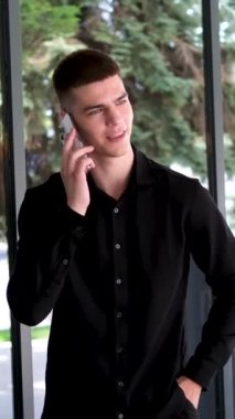 Sokakta kahve ve akıllı telefonlu şık bir gencin portresi. Siyah saçlı, mavi gözlü yakışıklı bir adam. Melez ırk uyruğu. Adam telefonda konuşuyor.