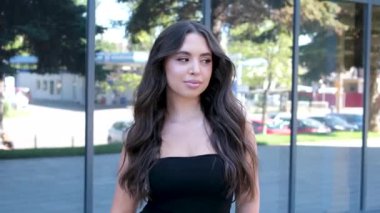 Güneşli bir günde modern ofis binasının önünde cam bir binanın arka planında duran bir iş kadını.