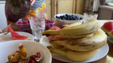 Mutfakta önlüklü bir kadın masa çileklerine, lokhina ahududu üzümlerine, eriklere ve muzlara ev yapımı limonata döküyor. Nane ve limonla su dök.
