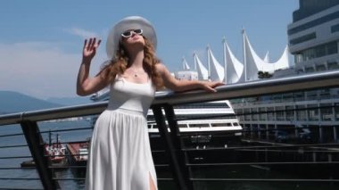 Gün batımında bir gemide güzel bir kadın. Beyaz şapkalı ve elbiseli ince bir kız Vancouver 'da Kanada' da bir rıhtımda duruyor.