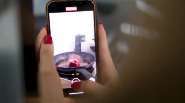 Kızartma tavasına biftek olarak ezilmiş sarımsak ve kekik ekliyorum. Kızartma tavasında et kızart. Blogcu kız cep telefonuyla yemek videoları çekiyor