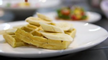 Kadınların elleri Belçika waffle 'ına muz dilimleri koyar. Kahvaltı hazırlığı. Tatlı yemek. muz waffle 'ları