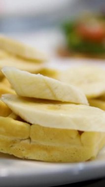 Kadınların elleri Belçika waffle 'ına muz dilimleri koyar. Kahvaltı hazırlığı. Tatlı yemek. muz waffle 'ları