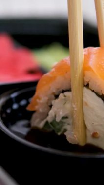 Sopalar suşi kutusundan suşi alır, yakın plan. Plastik bir kutuda yuvarlanıyor. Çeşitli lezzetli Japon suşilerinden oluşan hazır yemek seti teslimat konteynerinde. Sağlıklı beslenme, Asya yemekleri, hazır yemek.