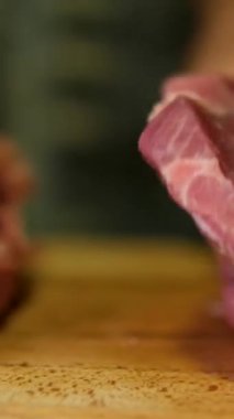 Baharatlı biftek pişirme süreci ve ahşap mutfak masasında otlar, üzerine deniz tuzu ve biber serpiştirme süreci. Adım adım, bir adam biftekleri doğruyor ve kızartma tavasında kızartıyor.