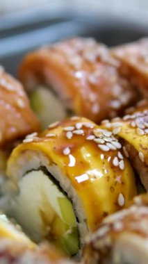 Sopalar suşi kutusundan suşi alır, yakın plan. Plastik bir kutuda yuvarlanıyor. Çeşitli lezzetli Japon suşilerinden oluşan hazır yemek seti teslimat konteynerinde. Sağlıklı beslenme, Asya yemekleri, hazır yemek.