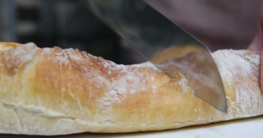 Ekmek. Fransız ekmeği. Ev yapımı ekmek somunu bir mutfak aşçısı tarafından kesme tahtasına dilimleniyor. Fırında pişirdikten sonra. Arka planda peynir ve şarap var. Eylem görüntüsü. 