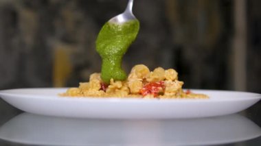Şef genovese pesto soslu makarnayı siyah masaya yakın plan malzemelerle ekliyor.