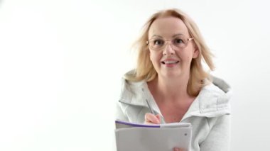 Gözlüklü, kalem ve defter takan yetişkin bir kadın ilginç bir şekilde gülümseyen beyaz saçlı, kıvırcık saçlı, neşeli bir kalem yetiştirme fikri var. Sportif gri kazak