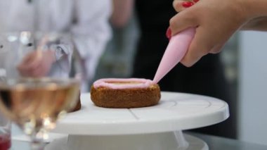 Kadın elleri pembe kremayı güzel bir pembe pastadaki spatulayla aynı seviyeye getiriyor. Kürsüdeki bir kız için doğum günü pastası. Pembe pasta yapan kız.