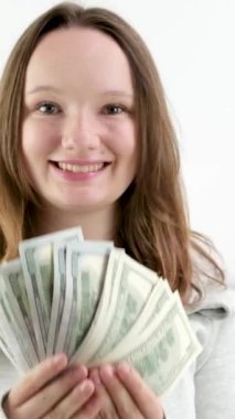 Genç ve mutlu bir kız 100 dolarlık banknotlar gibi para sallıyor. Ağzı açık gülüyor. Sürpriz sevinç. Beyaz arka plan spor giyim. Avrupa Dili