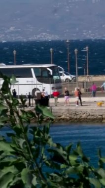 Turizm şirketi Virgin Voyages 'in otomobil otobüsleri kıyıda turistleri bekliyor. Akdeniz' deki bir yolcu gemisinin arka planında deniz otobüsleri yüzüyor. Mykonos 11.24.2024