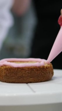 Kadın elleri pembe kremayı güzel bir pembe pastadaki spatulayla aynı seviyeye getiriyor. Kürsüdeki bir kız için doğum günü pastası. Pembe pasta yapan kız.