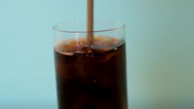 Köpüklü içecek kokteyli ya da bardağa saman içerek karıştırılan kola. Buzlu baloncuklar. Gaz bardaktan çıkar, arka planda parlayan damlacıklar. Pipetle buz karıştırılmış kola.