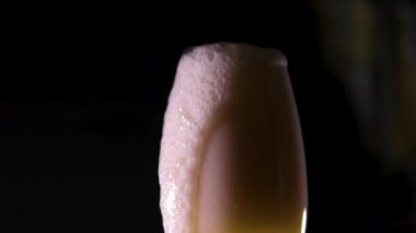 Bardağa bira dolduruyorum. Bira köpüğü dolup taşar ve siyah arkaplanda biter. 