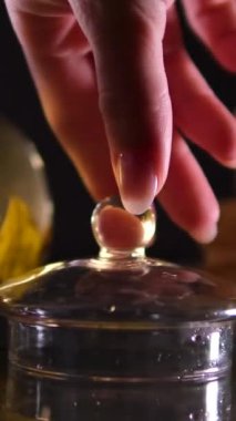 Bir kadın eli çaydanlığı kaplar, çay cam bir çaydanlıkta demlenir çiçeklerle ve ıhlamur yapraklarıyla arka planda. Çay demleme ya da demleme sürecinin videosu