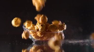Tatlı karamelli patlamış mısır siyah arka planda bir bardağa dökülüyor, ağır çekimde. Karamelli patlamış mısır
