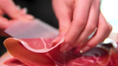 Pişmiş çiğ jambon, dönüyor. Bir dilim prosciutto Crudo, İtalyan yemeği. Domuz eti kurutulmuş jambon. Antipasto, salam. Kadın eli, jambon dilimlerini tahtanın üzerinde servis yapmaktan ayırıyor.