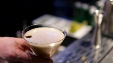 Adam masaya bir bardak espresso kokteyli koyuyor, yakın plan. Barda nefis bir espresso kokteyli, yakın plan. Ekspresso martini. Kokteyl ve kahve çekirdekleri masada.