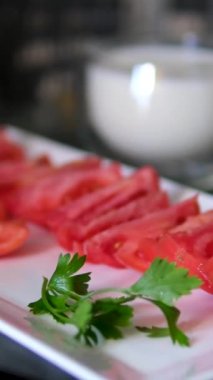 Taze dilimlenmiş domatesler maşayla beyaz bir tabakta, sıcak ışıkla aydınlatılmış mutfak ortamında servis edilmeye hazır. Beyaz tabakta domates dilimleri