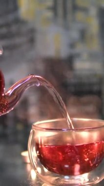 Beyaz arka planda cam çaydanlıkta kırmızı çay. Hibiscus şeffaf bir çift duvar camına dökülüyor. Tahta üzerinde dönen bitkisel çaylı çay fincanı. Amfibi boşalt