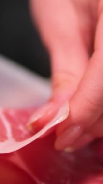 Pişmiş çiğ jambon, dönüyor. Bir dilim prosciutto Crudo, İtalyan yemeği. Domuz eti kurutulmuş jambon. Antipasto, salam. Kadın eli, jambon dilimlerini tahtanın üzerinde servis yapmaktan ayırıyor.