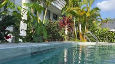 Berrak havuz kenarı, beyaz güneş pansiyonları ve yemyeşil yemyeşil verimli sakin ve davetkar bir tatil atmosferi yaratan lüks bir tropikal tatil beldesi.