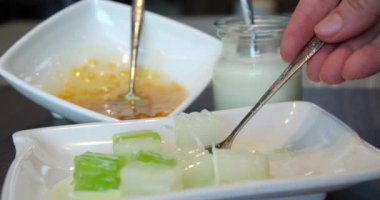 Geleneksel Endonezya aperatifi Es Campur 'la bir kaşık tutan bir kişi. Çim jölesi sergiliyor ve bu popüler tatlının canlandırıcı, renkli özelliklerini vurguluyor..