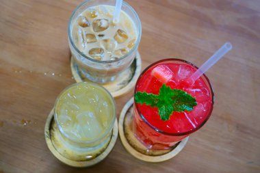 Pipetle şeffaf bardaklarda buzlu kahve, çay ve meyve suyu gibi çeşitli içecek seçenekleri. İçkiler renkli ve ferahlatıcı, çeşitli zevklere hitap ediyor..