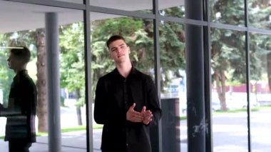 Dışarıdaki mutlu Hintli adam kameraya bakıyor. Gülümseyen mutlu, neşeli iş adamı ya da siyah tişörtlü, sakallı bir işçi ofis camının önünde dikiliyor.